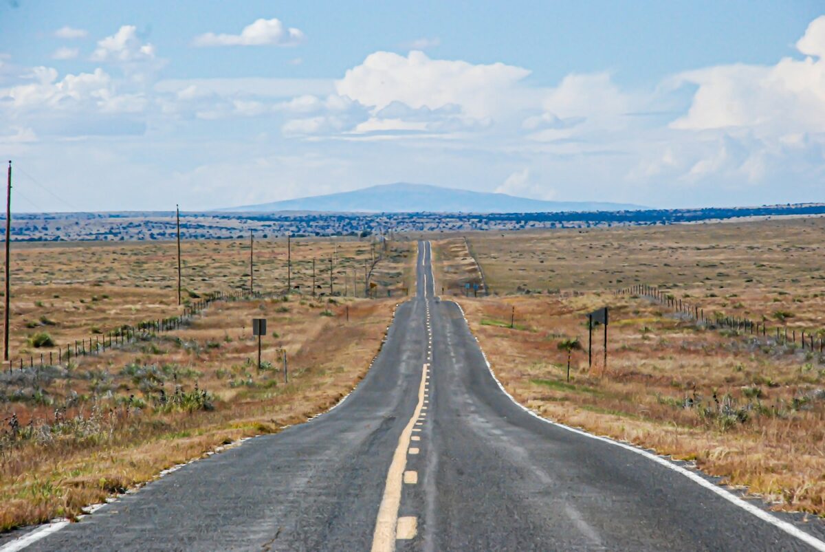 gray asphalt road between green grass field under blue sky during daytime